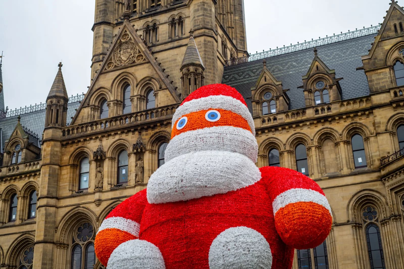 A large, illuminated Santa Claus figure in red and white stands in front of a historic stone building with Gothic architecture.